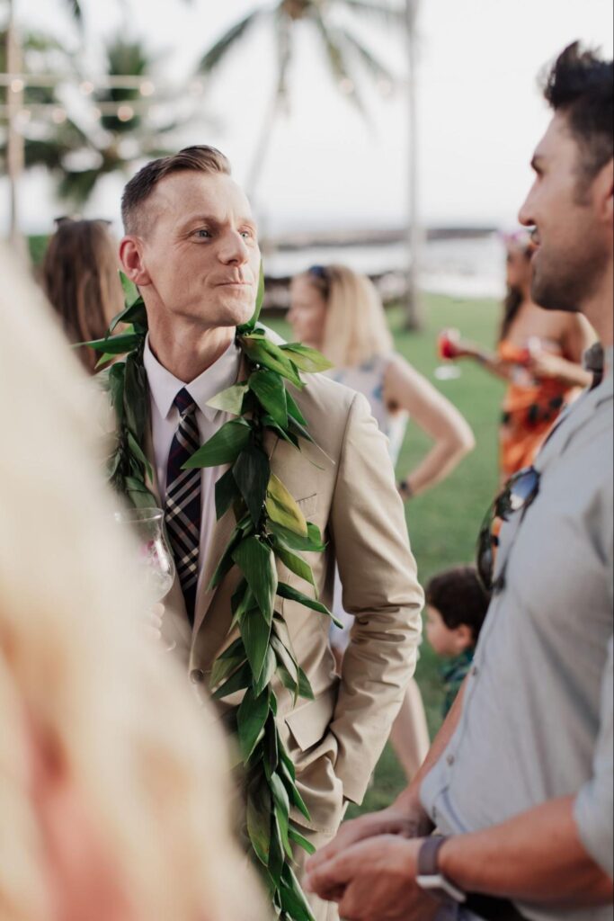 the groom wearing a lei and talking to a guest at his Maui wedding