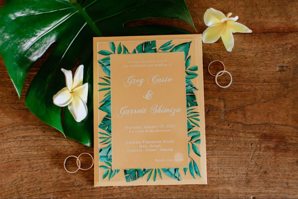 flat lay view of a wedding invitation beside wedding rings and flowers in Maui