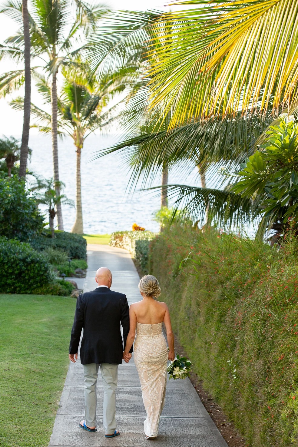 bride and groom holding hands walking down pathway away from camera Maui Hawaii