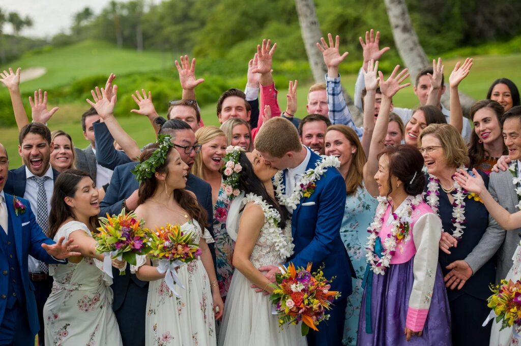 bride and groom kiss surrounded by family and friends cheering in Maui