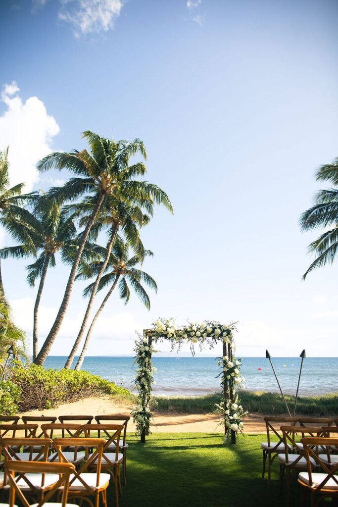 wedding arch with white flowers and greenery set against beach backdrop in Maui