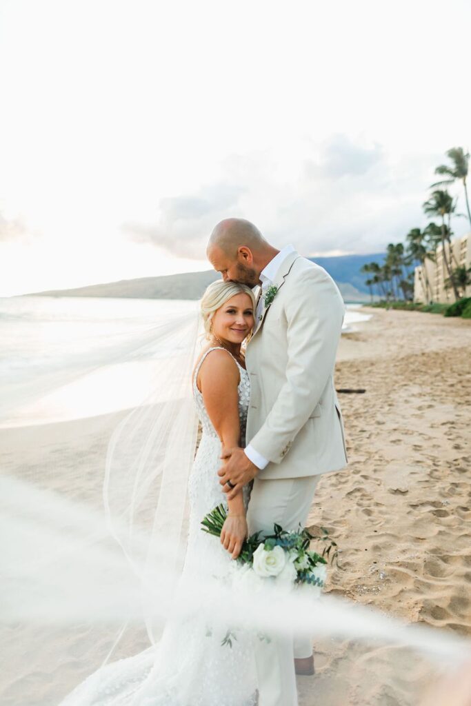 groom romantically kisses tops of brides head on Maui beach